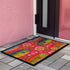 Rectangular indoor outdoor doormat featuring a vibrant hot pink background with a symmetrical maximalist pattern. The design showcases stylized sardines in yellow, lime green, and cobalt blue swimming horizontally towards a central vertical axis of blooming pale pink flowers and green vines. The imagery mimics the texture of vintage needlepoint embroidery but is a flat print on polyester. The mat is framed by a sleek black trim and features a non-slip rubber backing for safety.
