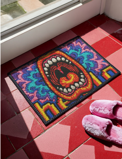A rectangular indoor and outdoor doormat featuring a vibrant, psychedelic design. The central graphic is a large, open screaming red and orange mouth with white teeth, surrounded by highly saturated wavy, trippy patterns in blue, purple, magenta, and teal. Yellow stylized text reading HELLO is integrated into the pattern. The mat has a smooth 2D flat print surface that mimics the look of textured chainstitch embroidery, finished with a solid black fabric trim around all four outer edges.