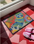 A rectangular outdoor doormat featuring a maximalist 2D print with a Trompe-l'œil embroidery effect. The central design depicts a blue and gold patterned raccoon wearing a green astronaut space helmet. The background is a vibrant red, filled with large, multi-colored folk art flowers in shades of pink, magenta, and gold with green leaves. The mat is finished with a sleek black border and has a textured surface mimicking high-fidelity raised needlepoint stitching.