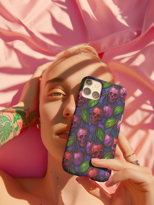 A protective phone case with a gothic cherry skull design featuring red and pink skulls blended with purple cherries and vibrant green leaves. The pattern is outlined in gold and set against a deep blue-purple stained glass background. The case has a smooth matte finish and fits various phone models with precision-cut camera openings.