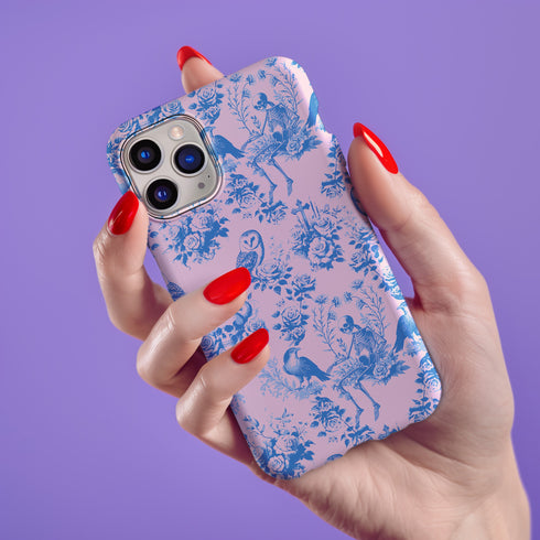 Phone case with pink background featuring blue toile print of skeletons, peacocks, owls, and roses. Victorian-inspired design with gothic elements. Dual-layer protection for various smartphone models.