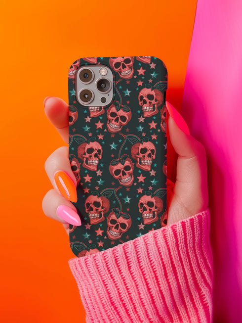 Phone case featuring coral pink apple skulls with green stems and multicolored stars on black background. Gothic alternative design with pastel accents.