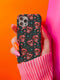 Phone case featuring coral pink apple skulls with green stems and multicolored stars on black background. Gothic alternative design with pastel accents.