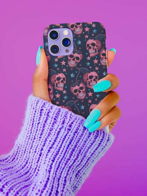 Phone case featuring coral pink apple skulls with green stems and multicolored stars on black background. Gothic alternative design with pastel accents.