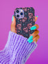 Phone case featuring coral pink apple skulls with green stems and multicolored stars on black background. Gothic alternative design with pastel accents.