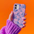 Phone case with pink background featuring blue toile print of skeletons, peacocks, owls, and roses. Victorian-inspired design with gothic elements. Dual-layer protection for various smartphone models.