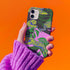 Colorful maximalist phone case with electric yellow tigers prowling through lush green tropical foliage. Psychedelic jungle theme on a purple backdrop. Bold summer design.
