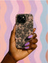Phone case with black lace floral design, soft pink satin bows, and small pearl accents on a pale nude background; fits iPhone, Samsung, and Pixel models