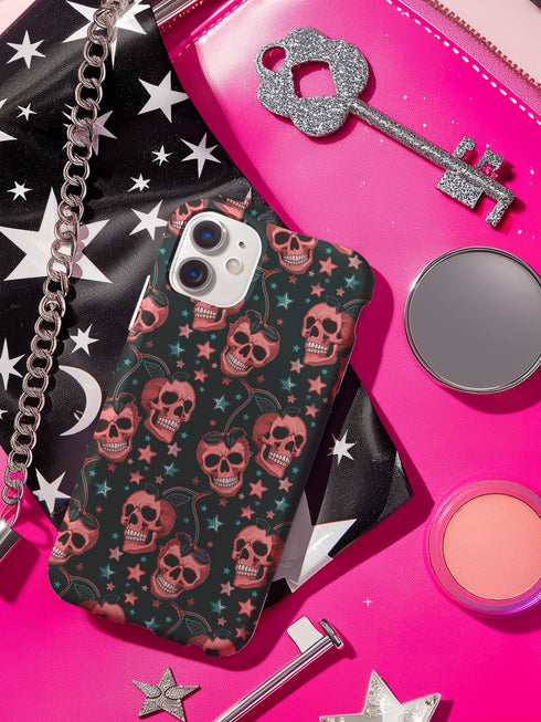 Phone case featuring coral pink apple skulls with green stems and multicolored stars on black background. Gothic alternative design with pastel accents.