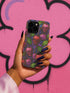 A protective phone case with a gothic cherry skull design featuring red and pink skulls blended with purple cherries and vibrant green leaves. The pattern is outlined in gold and set against a deep blue-purple stained glass background. The case has a smooth matte finish and fits various phone models with precision-cut camera openings.