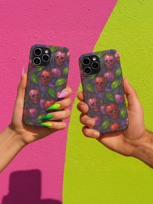 A protective phone case with a gothic cherry skull design featuring red and pink skulls blended with purple cherries and vibrant green leaves. The pattern is outlined in gold and set against a deep blue-purple stained glass background. The case has a smooth matte finish and fits various phone models with precision-cut camera openings.