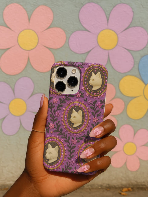 Pastel goth phone case with baroque cameo-style white cat heads framed by pearls and purple florals on a violet background; available for iPhone, Samsung, and Pixel models
