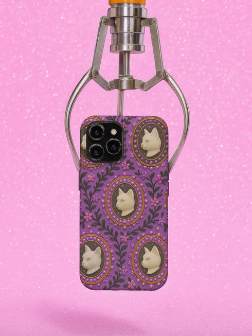Pastel goth phone case with baroque cameo-style white cat heads framed by pearls and purple florals on a violet background; available for iPhone, Samsung, and Pixel models