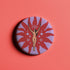 Circular pin featuring a nude goddess figure in gold against a red sunburst pattern on lavender background, with moon and star details