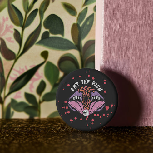 Black circular pin badge with purple fanged mouths design, psychedelic orange spiral, and "EAT THE RICH" text in white, scattered with red dots