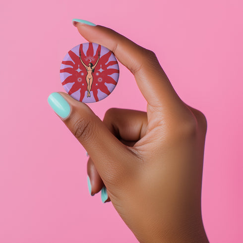 Circular pin featuring a nude goddess figure in gold against a red sunburst pattern on lavender background, with moon and star details