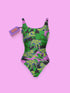A one-piece scoop neck swimsuit featuring a bold, all-over scattered print. The flat, 2D printed design has a solid black background overlaid with bright pink abstract shapes, medium green tropical leaves, and striking lime green tigers with dark navy blue stripes. The bathing suit features a low scoop back, cheeky fit bottom, wide shoulder straps, and a double-layer front with white lining inside. The fabric has zig-zag stitching along the edges.