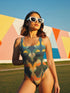 One-piece swimsuit featuring a bold 70s-inspired abstract pattern in deep navy, ochre, cream, orange, and green tones. The sculptural design creates a mirrored, psychedelic effect with curved shapes and layered swirls. Full coverage with scoop neckline and straps, ideal for retro beach looks and modern art goddesses.