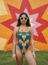 One-piece swimsuit featuring a bold 70s-inspired abstract pattern in deep navy, ochre, cream, orange, and green tones. The sculptural design creates a mirrored, psychedelic effect with curved shapes and layered swirls. Full coverage with scoop neckline and straps, ideal for retro beach looks and modern art goddesses.