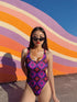 Bold patterned one-piece swimsuit with retro evil eye floral design, styled in festival-ready outdoor settings. Swimsuit features a scoop neckline, cheeky fit, and low scoop back. Ideal for summer vacations, pool parties, raves, and alt girl fashion. Made from stretchy, moisture-wicking fabric with UPF 50+ protection. Available in sizes XS to 3X. Colorful, statement swimwear designed for confident, maximalist style lovers.