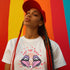White t-shirt featuring a surreal, psychedelic design centered on the chest. An open mouth with sharp vampire-like teeth and pink tongue dominates the image. Between the teeth, a hypnotic swirling pattern in rainbow colors leads to a single eyeball on the tongue. "EAT THE RICH" is written in white above the mouth. Red paint-like splatters surround the entire design, giving it a grungy, punk aesthetic. The shirt is from the "Honey Dazed" brand.