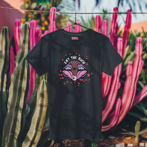 Black t-shirt featuring a surreal, psychedelic design centered on the chest. An open mouth with sharp vampire-like teeth and pink tongue dominates the image. Between the teeth, a hypnotic swirling pattern in rainbow colors leads to a single eyeball on the tongue. "EAT THE RICH" is written in white above the mouth. Red paint-like splatters surround the entire design, giving it a grungy, punk aesthetic. The shirt is from the "Honey Dazed" brand.