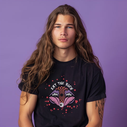 White t-shirt featuring a surreal, psychedelic design centered on the chest. An open mouth with sharp vampire-like teeth and pink tongue dominates the image. Between the teeth, a hypnotic swirling pattern in rainbow colors leads to a single eyeball on the tongue. "EAT THE RICH" is written in white above the mouth. Red paint-like splatters surround the entire design, giving it a grungy, punk aesthetic. The shirt is from the "Honey Dazed" brand.
