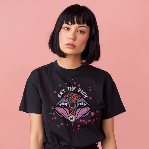 T-shirt featuring a surreal, psychedelic design centered on the chest. An open mouth with sharp vampire-like teeth and pink tongue dominates the image. Between the teeth, a hypnotic swirling pattern in rainbow colors leads to a single eyeball on the tongue. "EAT THE RICH" is written in white above the mouth. Red paint-like splatters surround the entire design, giving it a grungy, punk aesthetic. The shirt is from the "Honey Dazed" brand.