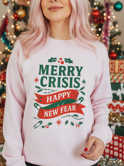 A holiday sweatshirt in pink or red with a punk and goth aesthetic. The text reads "MERRY CRISIS" and "HAPPY NEW FEAR" in a bold, gothic-style font. The design is decorated with holly leaves, berries, thorny vines, and safety pins, all arranged in a festive but alternative holiday style. This funny goth Christmas pullover is a sarcastic statement piece, perfect as dark humor apparel for the winter season.
