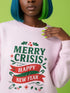 A holiday sweatshirt in pink or red with a punk and goth aesthetic. The text reads "MERRY CRISIS" and "HAPPY NEW FEAR" in a bold, gothic-style font. The design is decorated with holly leaves, berries, thorny vines, and safety pins, all arranged in a festive but alternative holiday style. This funny goth Christmas pullover is a sarcastic statement piece, perfect as dark humor apparel for the winter season.
