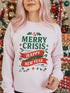 A holiday sweatshirt in pink or red with a punk and goth aesthetic. The text reads "MERRY CRISIS" and "HAPPY NEW FEAR" in a bold, gothic-style font. The design is decorated with holly leaves, berries, thorny vines, and safety pins, all arranged in a festive but alternative holiday style. This funny goth Christmas pullover is a sarcastic statement piece, perfect as dark humor apparel for the winter season.