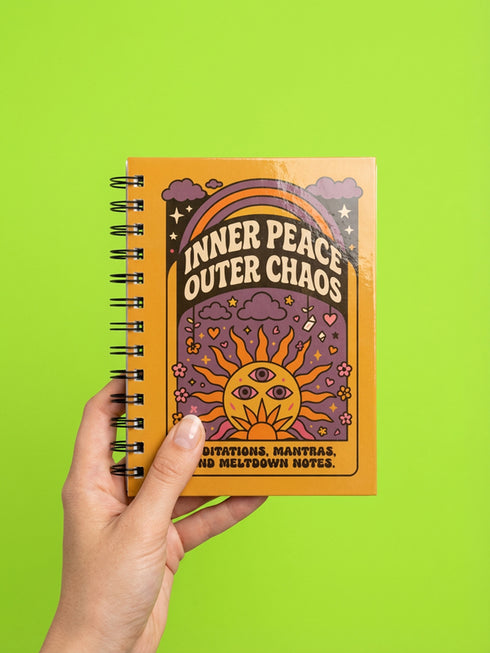 A glossy 5x7 inch spiral bound notebook featuring the phrase Inner Peace Outer Chaos in retro 70s typography. The cover showcases a vibrant psychedelic design on a mustard yellow background with a central trippy sun motif containing three mystical eyes. Below the sun, text reads Meditations, Mantras, and Meltdown Notes in bold black font. The journal has a durable black metal spiral binding and contains 150 lined pages for writing, shadow work, or daily planning.