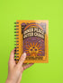 A glossy 5x7 inch spiral bound notebook featuring the phrase Inner Peace Outer Chaos in retro 70s typography. The cover showcases a vibrant psychedelic design on a mustard yellow background with a central trippy sun motif containing three mystical eyes. Below the sun, text reads Meditations, Mantras, and Meltdown Notes in bold black font. The journal has a durable black metal spiral binding and contains 150 lined pages for writing, shadow work, or daily planning.