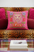 Maximalist throw pillow for the Leo zodiac sign featuring a centralized lion head medallion with an ornate mane mimicking embroidered textures. The background is a vibrant hot pink, accented by ochre, rust, and lime green floral motifs and blue flowers in each corner. The pillow is square with a hidden zipper and a polyester insert. This high-contrast design is a perfect fit for dopamine decor, whimsigoth apartments, or any eclectic home looking for a bold astrology-inspired statement piece.