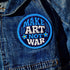 Round embroidered iron-on patch featuring "MAKE ART NOT WAR" text with blue floral design. Navy blue background with light blue border, white cream lettering, and small yellow-centered blue flowers. 3-inch circular twill fabric patch perfect for jackets, backpacks, denim, and clothing customization. Anti-war peace activist feminist punk alternative accessory for creative counterculture gift giving.