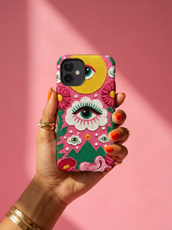 Maximalist phone case with a vibrant hot pink background featuring a faux crochet knit texture illusion. The design includes a large yellow crescent moon with a green eye in the top right, a central white cloud with a green eye and red lashes, and green mountain peaks at the bottom. Red flowers and pink swirling mist accent the scene.