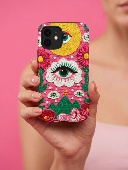 Maximalist phone case with a vibrant hot pink background featuring a faux crochet knit texture illusion. The design includes a large yellow crescent moon with a green eye in the top right, a central white cloud with a green eye and red lashes, and green mountain peaks at the bottom. Red flowers and pink swirling mist accent the scene.