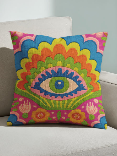 Polyester faux embroidered pillow cover featuring a bold maximalist evil eye design with a colorful folk-art inspired pattern. The front print includes a central blue, green, and pink eye surrounded by scalloped floral shapes, rainbow-like arches, leafy details, and bright decorative flowers in pink, orange, yellow, blue, and green. Soft square pillow cover with a textured woven-look print. Available in 18x18 or 22x22 inches.