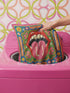 Maximalist throw pillow cover featuring a printed faux embroidery design with red open lips, pink tongue, white teeth, green scalloped medallion border, yellow and pink flowers, and decorative folk-inspired bands on a bright blue background with hot pink edging. Square colorful pillowcase for eclectic home decor, retro interiors, dopamine decor, boho living rooms, statement sofas, beds, chairs, and reading nooks.