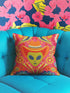 A vibrant pink square throw pillow featuring a green alien head wearing an orange cowboy hat. The alien is surrounded by colorful retro floral patterns in yellow, blue, and red. The style combines space cowgirl aesthetic with maximalist dopamine decor. The fabric has a premium linen texture. The cushion sits on a bright blue sofa, showcasing its bold, funky design. Perfect for weirdcore, sci-fi, or western themed rooms.