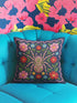 Square throw pillow cover featuring a symmetrical folk art spider illustration centered on a large hot pink flower. The spider has a striped abdomen in green, red, and yellow with pink legs. The background is a textured dark navy blue fabric with a visible faux linen weave. Surrounding the central spider are stylized botanical motifs including red daisies, blue forget-me-nots, and green leaves. The illustration is flat printed with a high-quality finish. This image shows the case only.