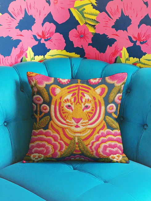 Square decorative throw pillow cover featuring a vibrant, maximalist illustration of a walking tiger surrounded by blooming pink peonies and green foliage. The design is set against a deep teal-charcoal background and mimics the texture of vintage hand embroidery with a faux-stitch printed effect. The style blends Junglecore, Chinoiserie, and Whimsigoth aesthetics. The fabric is a durable, linen-textured spun polyester. The tiger is orange, gold, and black; flowers are magenta pink.