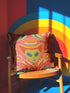 A vibrant pink square throw pillow featuring a green alien head wearing an orange cowboy hat. The alien is surrounded by colorful retro floral patterns in yellow, blue, and red. The style combines space cowgirl aesthetic with maximalist dopamine decor. The fabric has a premium linen texture. The cushion sits on a bright blue sofa, showcasing its bold, funky design. Perfect for weirdcore, sci-fi, or western themed rooms.