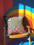 Square throw pillow cover with a faux embroidery 2D print of a stylized folk-art serpent with a blue head, yellow swirl markings, red eyes, white fangs, and an open red mouth. It is surrounded by pink, purple, and white flowers with yellow centers and green leaves on a deep blue background. The print mimics raised stitching while staying flat and smooth, and shows on both sides. Cover only, available in 18 by 18 inch and 22 by 22 inch sizes.