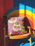 Square throw pillow cover packed with a dense repeating pattern of cat faces in hot pink, lime green, purple, and white, every cat wearing oversized retro sunglasses. Wavy psychedelic bands of orange, yellow, and green weave through the background. The flat 2D print mimics heavy textured crewel needlepoint on a smooth, linen-feel fabric. Reversible same design front and back with a hidden zipper. Funky maximalist cat decor and quirky apartment warming gift, available in 18 by 18 inch and 22 by 22 inch, cove
