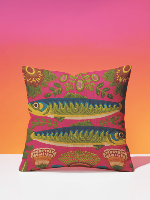 A square throw pillow cover featuring a symmetrical maximalist design on a hot pink background. Two stylized green and blue sardines swim in opposite directions in the center, featuring detailed scales and yellow eyes. The fish are surrounded by a folk art style pattern of green leafy vines and stylized orange and yellow flowers at the corners. The fabric has a faux linen texture with a flat printed design that mimics the look of vintage embroidery. Vibrant colors include pink, green, blue.