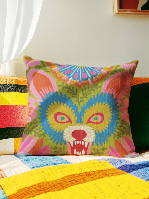 A square throw pillow cover featuring a vibrant, symmetrical illustration of an angry opossum face. The design mimics the texture of folk art embroidery but is a smooth flat print on faux linen fabric. The possum features teal blue fur, bright yellow eyes with pink pupils, and a red nose, bearing sharp white teeth in a hiss or scream. The background is a mossy green with pink and orange floral accents surrounding the animal. The style is maximalist, eclectic, colorful, and feral core aesthetic.