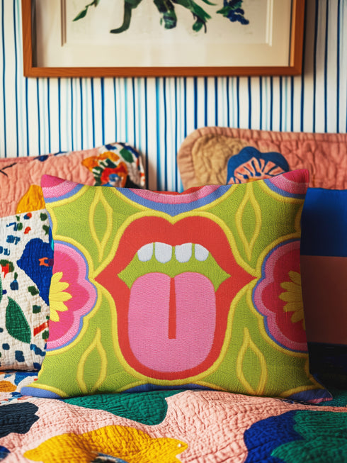 A square decorative throw pillow cover featuring a bold, symmetrical pop art design of an open mouth with bright red lips, white teeth, and a pink tongue sticking out. The central graphic is set against a lime green background surrounded by abstract geometric and floral shapes in vibrant hues of pink, yellow, and cornflower blue. The fabric has a visible premium linen-like woven texture. The colorful retro illustration is printed on both sides of the pillowcase.