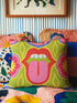 A square decorative throw pillow cover featuring a bold, symmetrical pop art design of an open mouth with bright red lips, white teeth, and a pink tongue sticking out. The central graphic is set against a lime green background surrounded by abstract geometric and floral shapes in vibrant hues of pink, yellow, and cornflower blue. The fabric has a visible premium linen-like woven texture. The colorful retro illustration is printed on both sides of the pillowcase.