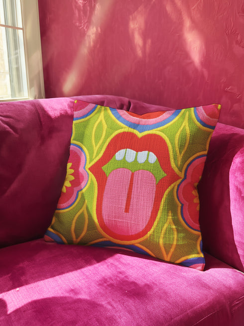 A square decorative throw pillow cover featuring a bold, symmetrical pop art design of an open mouth with bright red lips, white teeth, and a pink tongue sticking out. The central graphic is set against a lime green background surrounded by abstract geometric and floral shapes in vibrant hues of pink, yellow, and cornflower blue. The fabric has a visible premium linen-like woven texture. The colorful retro illustration is printed on both sides of the pillowcase.